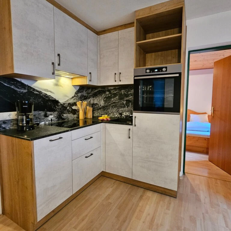 Moderne Küche in der Ferienwohnung des Hinterrohrguts in Flachau mit Backofen und Bergmotiv-Rückwand.